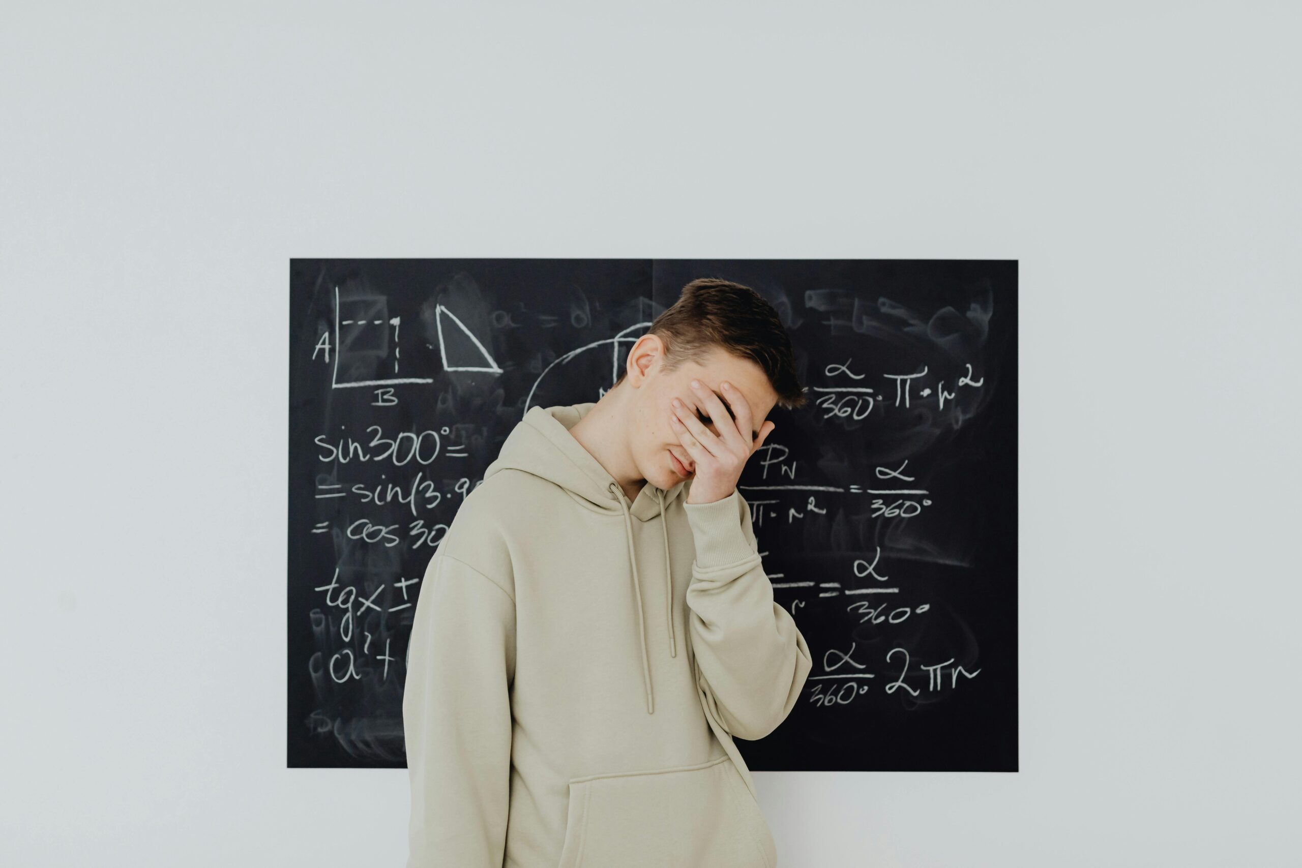 adolescent avec sa main sur les yeux devant un tableau rempli de formules mathématiques